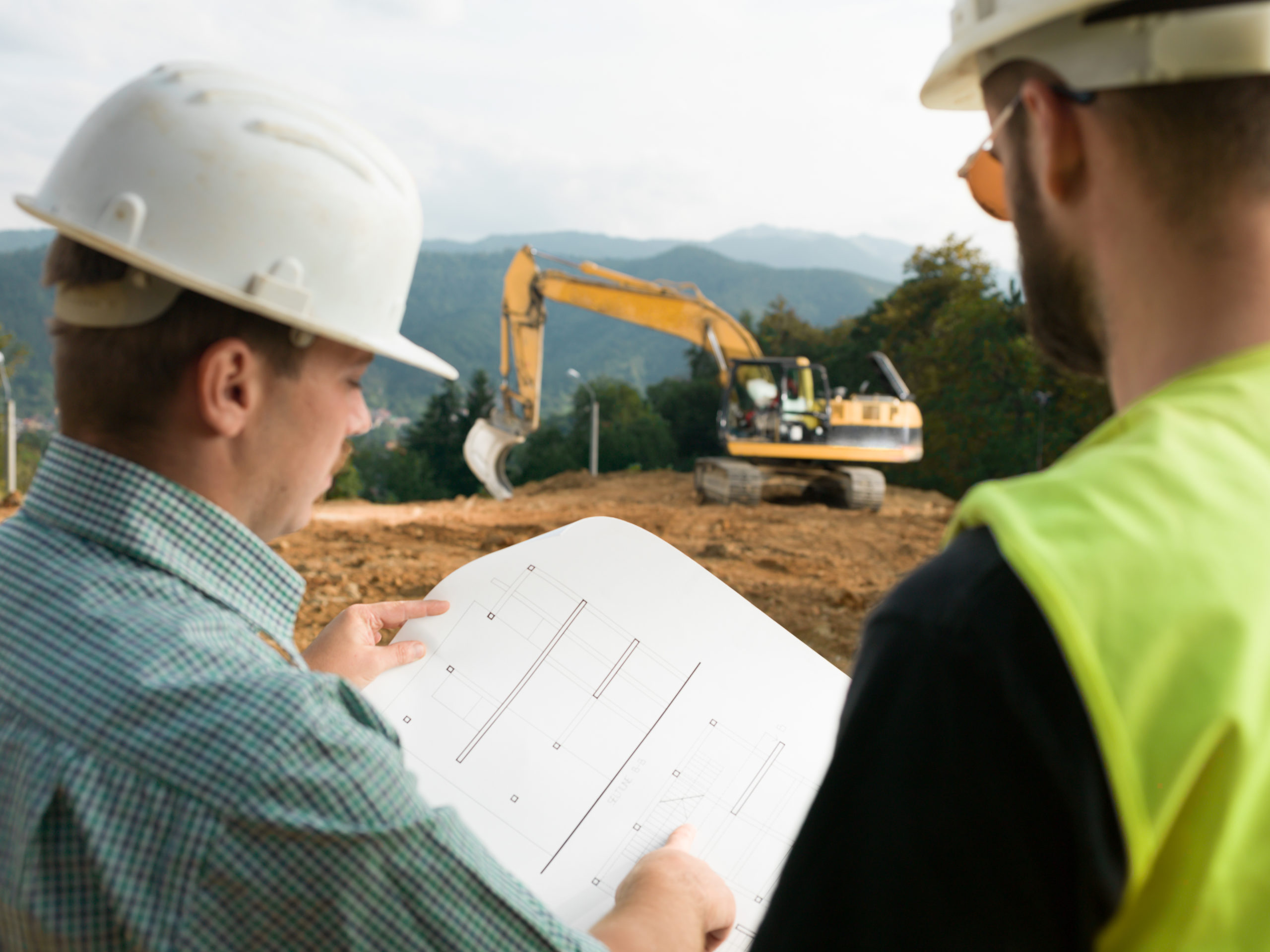 two men reviewing documents while construction is performed in distance