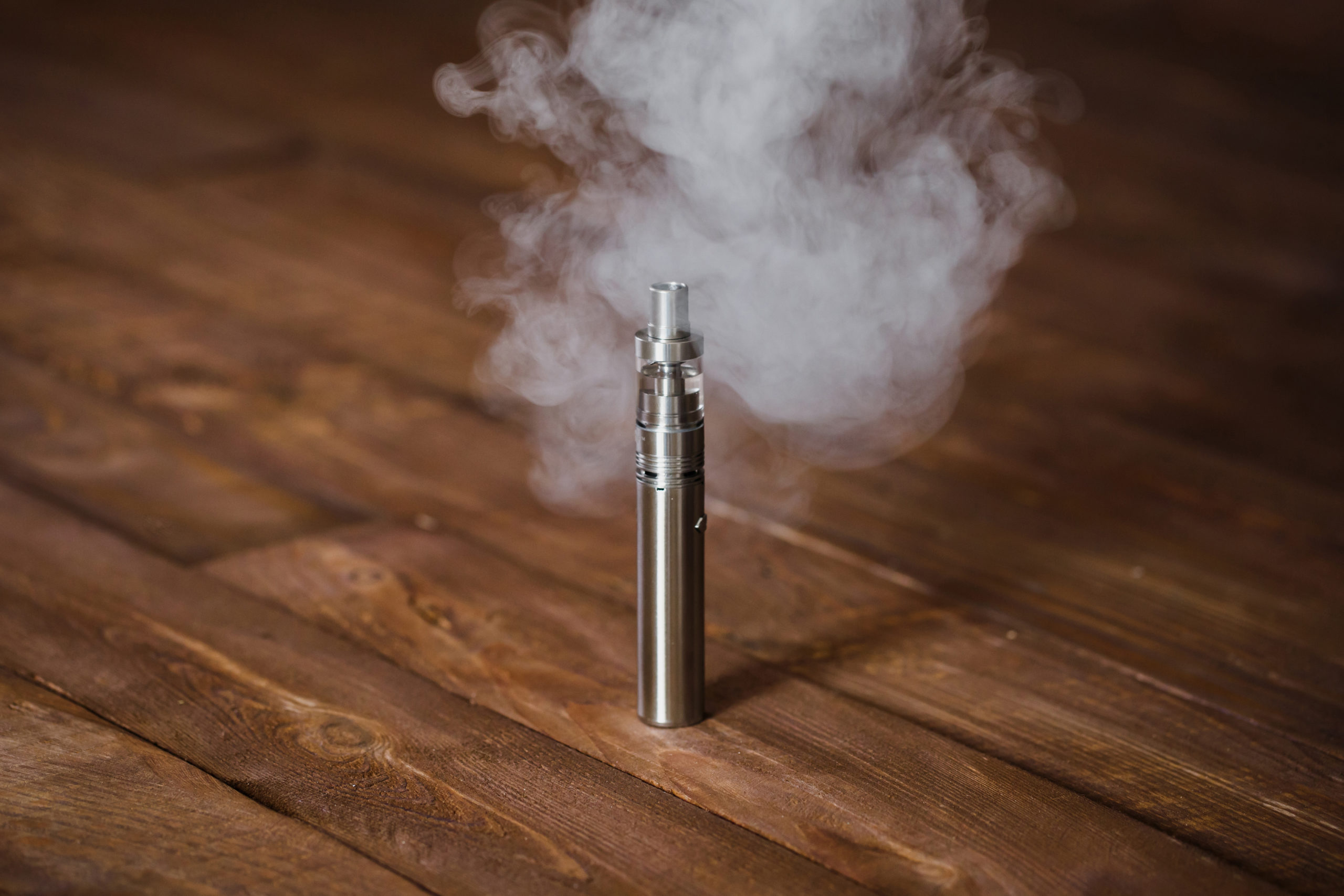 Electronic cigarette or an E-cigarette in a wooden table with smoke coming out the top piece and sides