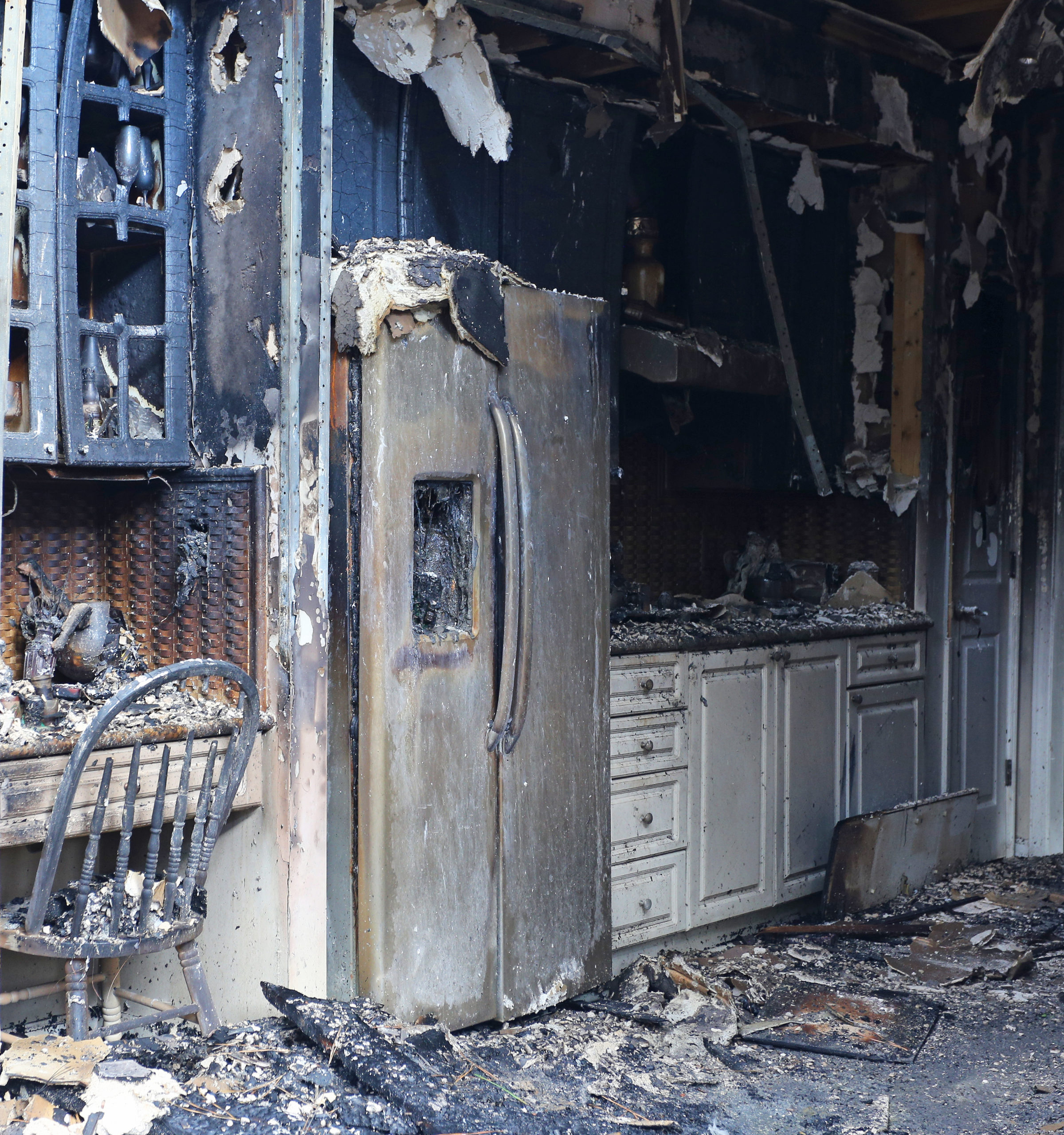 Image of the interior of a home or office following a fire showing burned walls, appliances, cabinets and storage, and chairs